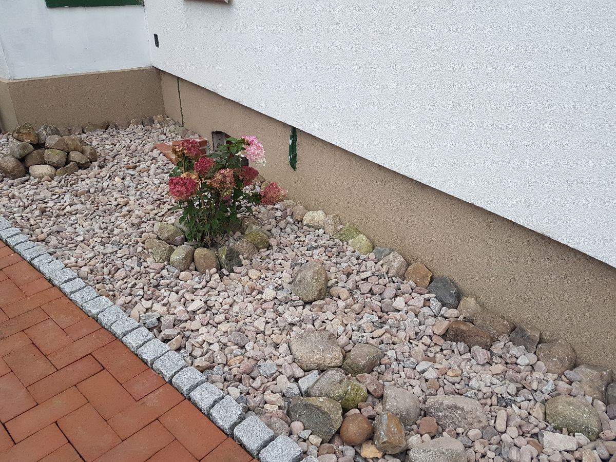 Beet mit Findlingen und Rosen entlang der gepflasterten Zufahrt