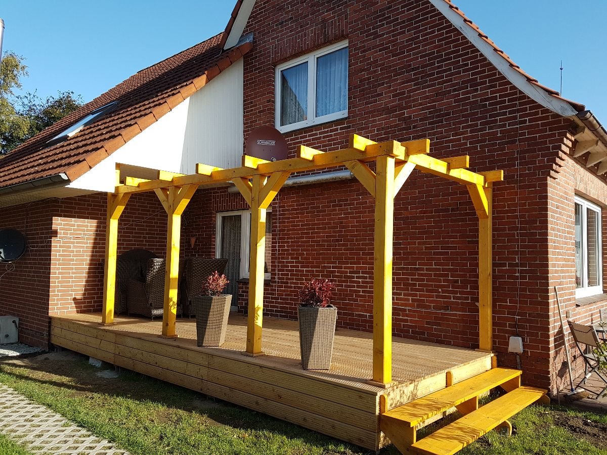 Neu gebaute Holzpergola über einer Terrasse an einem Backsteinhaus