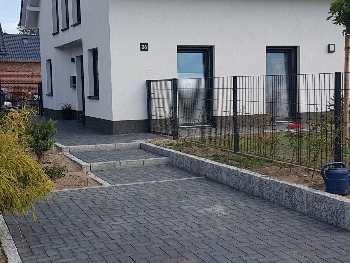 Neu gepflasterte Einfahrt mit Granit-Randsteinen vor einem weißen Wohnhaus